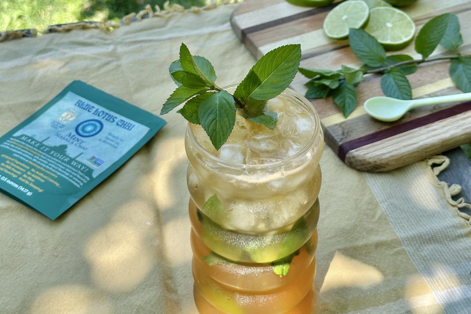 Chai mojito glass with a pouch of blue lotus chai, slices of lime and a mint sprig on a cutting board.