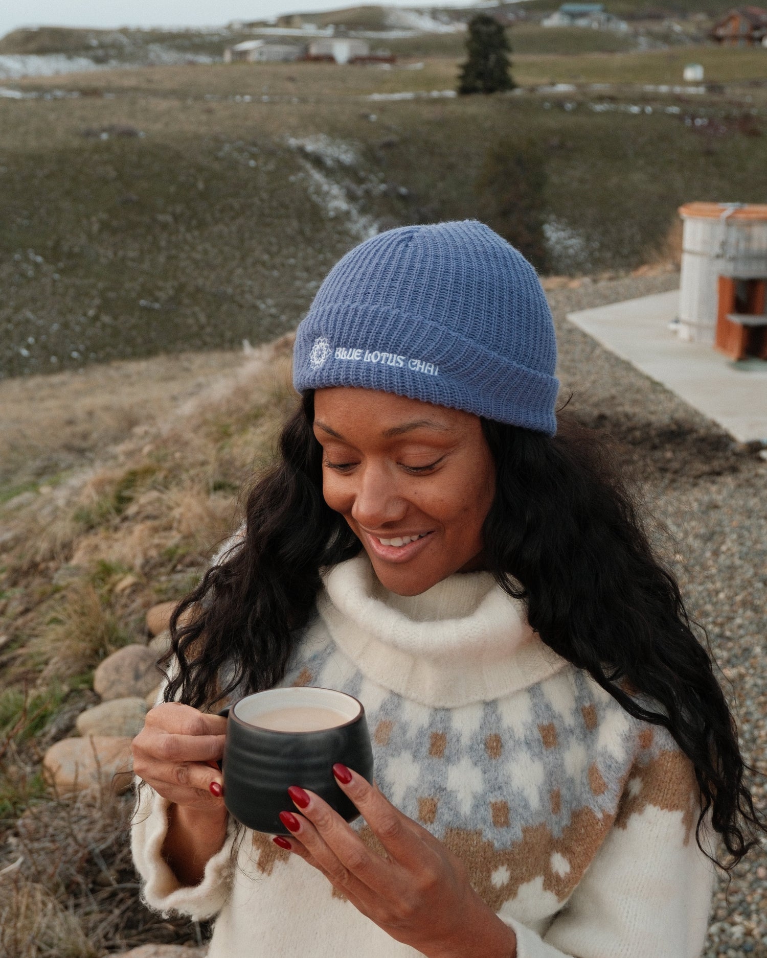 Woman in a blue beanie and white sweater holding a mug of blue lotus chai