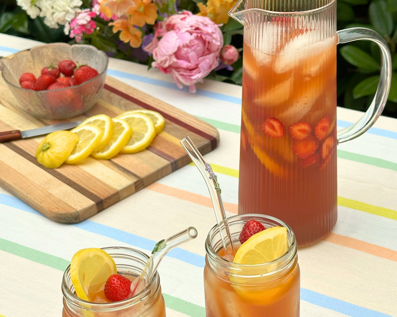 Two jars and a pitcher of chai spiced strawberry lemonade on a picnic table.